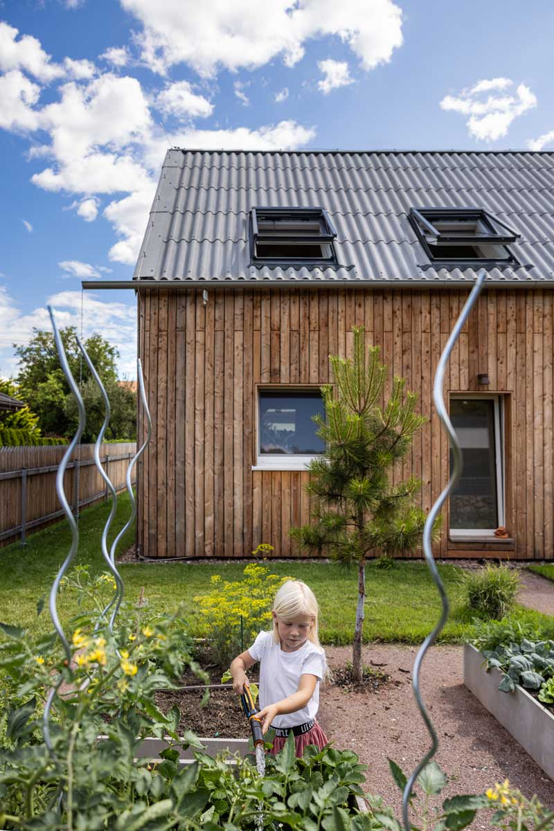 Vyvýšené záhony u udržitelné dřevostavby s fasádou ze sibiřského modřínu a sedlovou střechou