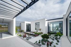 Atrium domu s úzkým vodním kanálem, betonovými stupni a výsadbou v bílém kačírku.