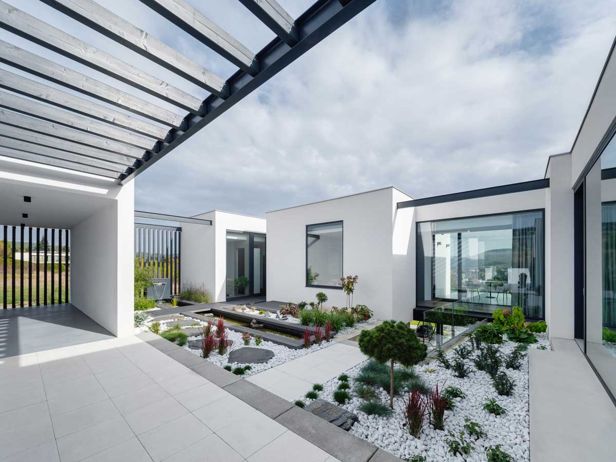 Atrium domu s úzkým vodním kanálem, betonovými stupni a výsadbou v bílém kačírku.