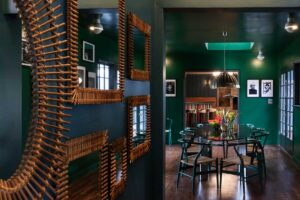 Zrcadlová stěna s výrazným rámem odráží tmavě zelený interiér a násobí hloubku i atmosféru prostoru.