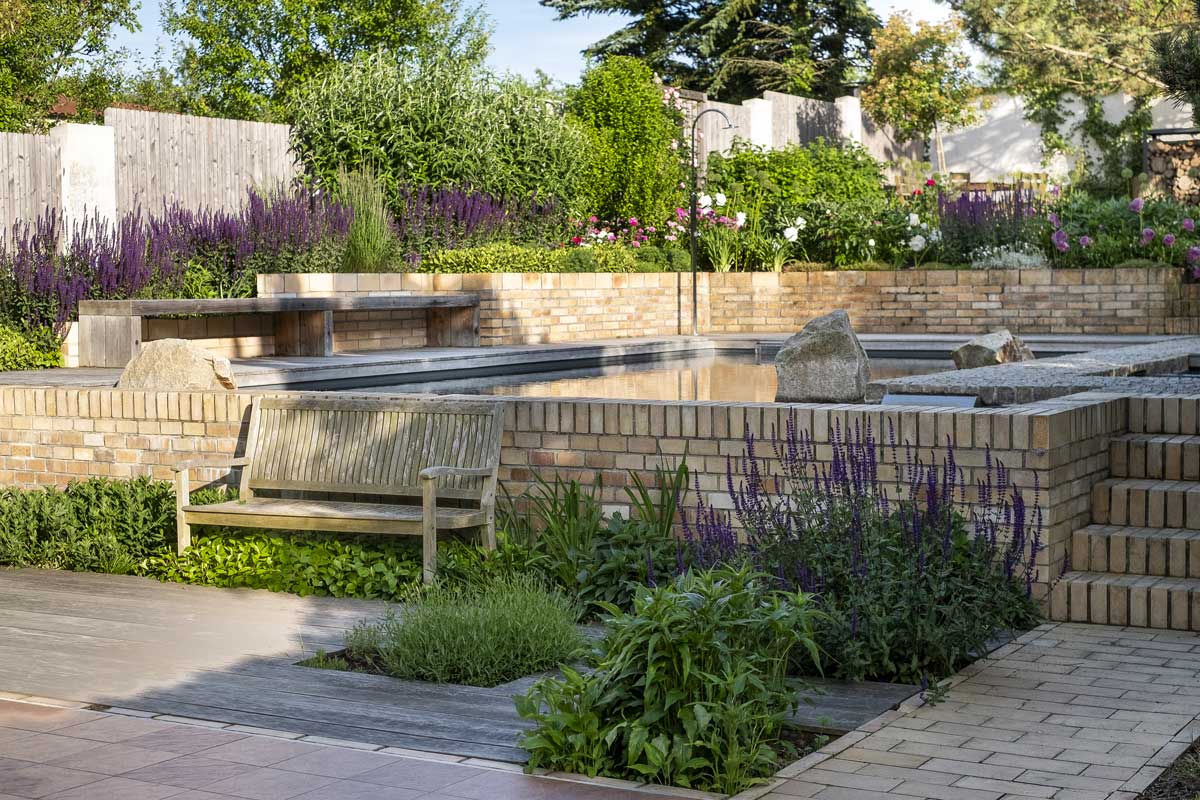 Zahrada se strukturovanou výsadbou a vodním prvkem, která působí přirozeně a harmonicky