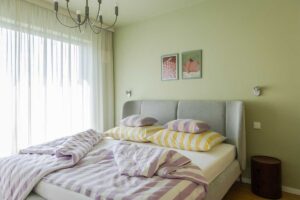 Ložnice pracuje s tlumenou zelenou stěnou a textiliemi v jemných žlutých a fialových tónech, které působí uklidňujícím dojmem.