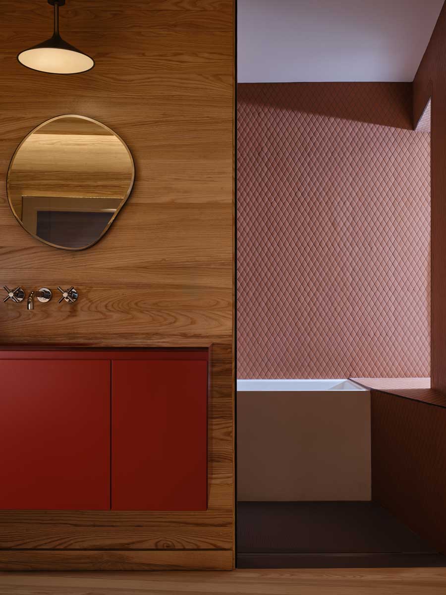 Koupelna s červenou skříňkou, dřevem a vanou v útulném, tlumeném prostoru