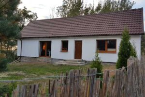 Zrekonstruovaný dům se světlou fasádou a sedlovou střechou obklopený zelení