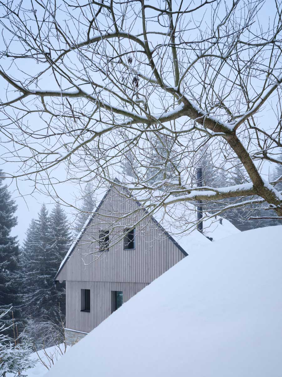 Chalupa zasazená do hlubokého sněhu ve strmém svahu