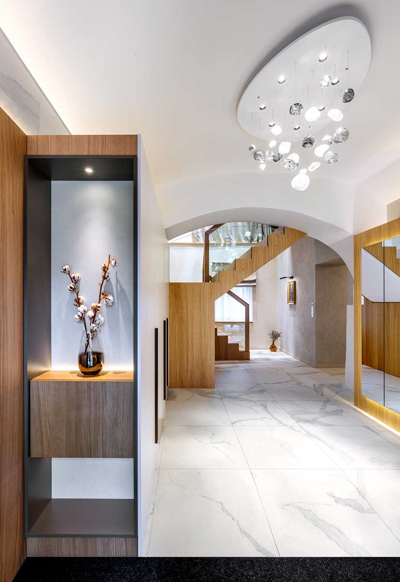 Vstupní část bytu s oblými klenbami podsvícenou zrcadlovou stěnou a nábytkem vyrobeným na míru.