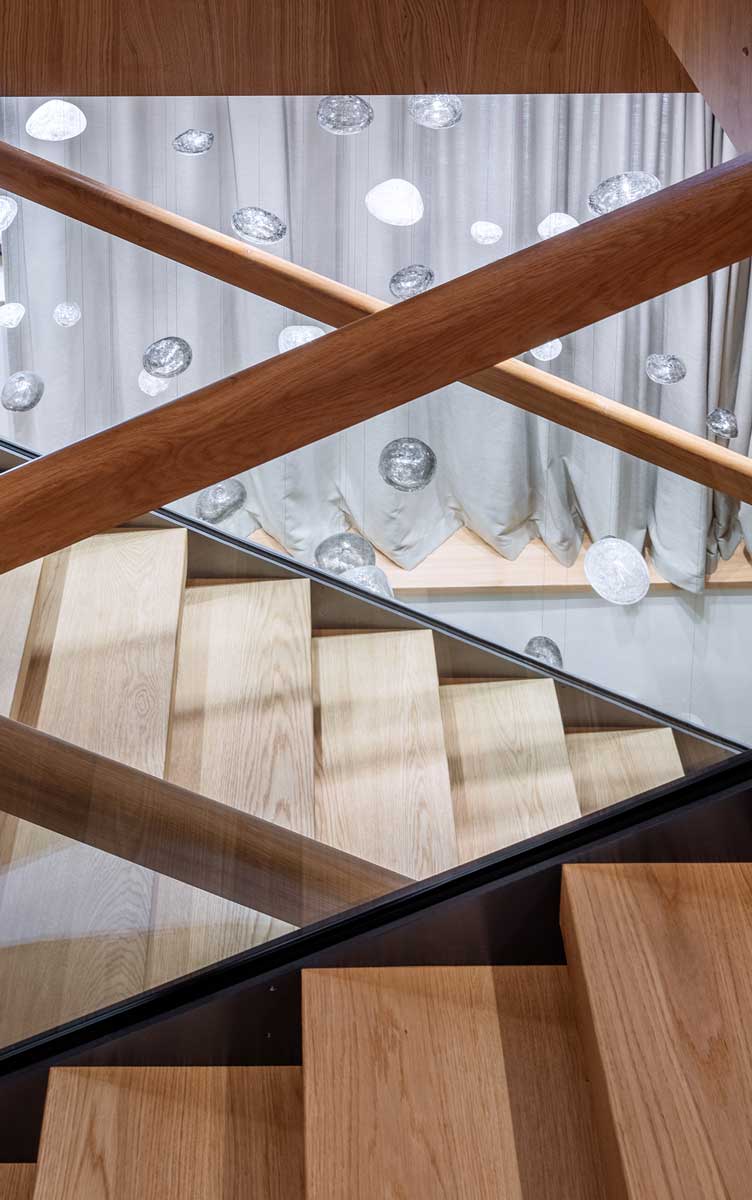 Detail dřevěného schodiště s proskleným zábradlím a skleněnou plastikou připomínající mraky.