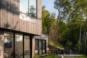 Zahrada s kamennými šlapáky a posezením u domu ve svahu obklopeného lesem.