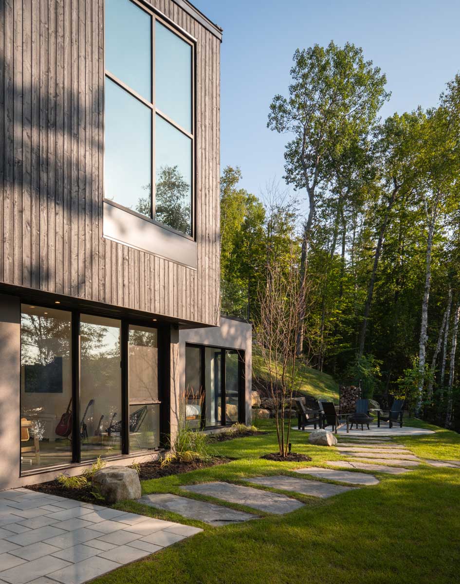 Zahrada s kamennými šlapáky a posezením u domu ve svahu obklopeného lesem.