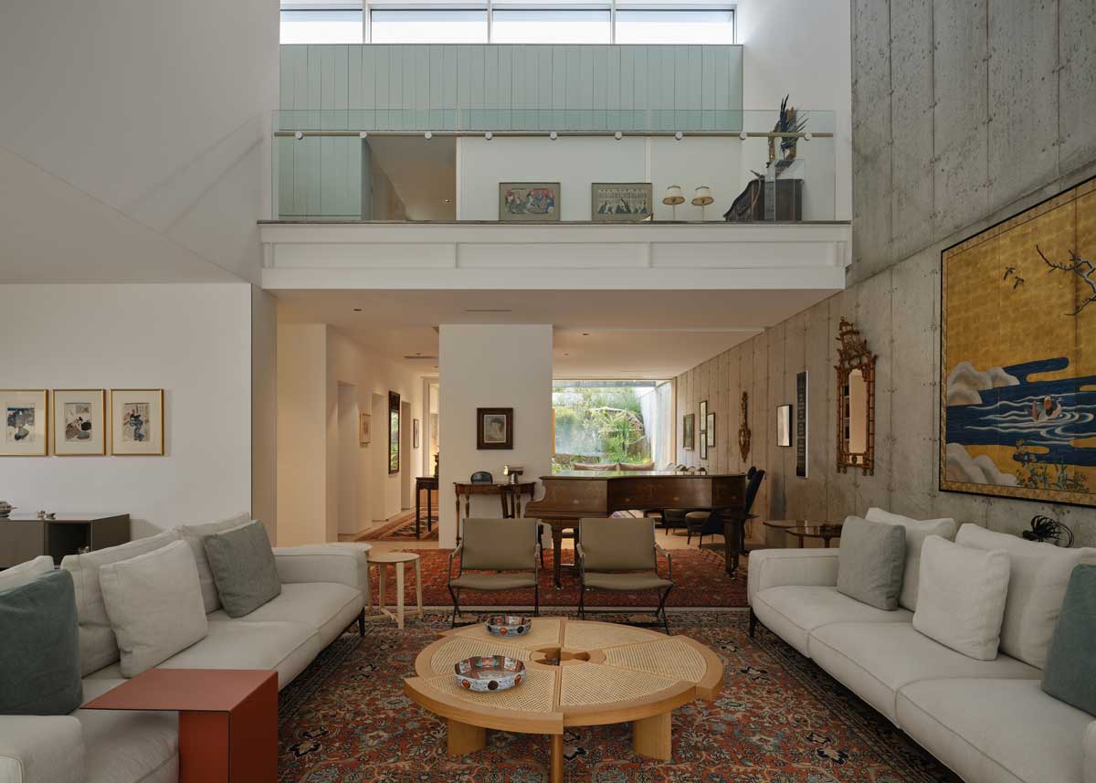 Prostorný obývací pokoj s vysokým stropem, galerií a kombinací betonu a dřeva Titulek: Otevřený prostor propojuje jednotlivé funkce domu a zároveň zachovává pocit