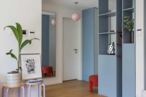 Pohled přes obývací část směrem ke vstupu ukazuje knihovnu na míru, barevné akcenty a otevřenou dispozici bytu.