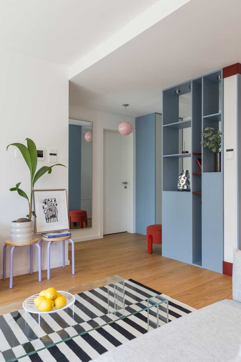 Pohled přes obývací část směrem ke vstupu ukazuje knihovnu na míru, barevné akcenty a otevřenou dispozici bytu.
