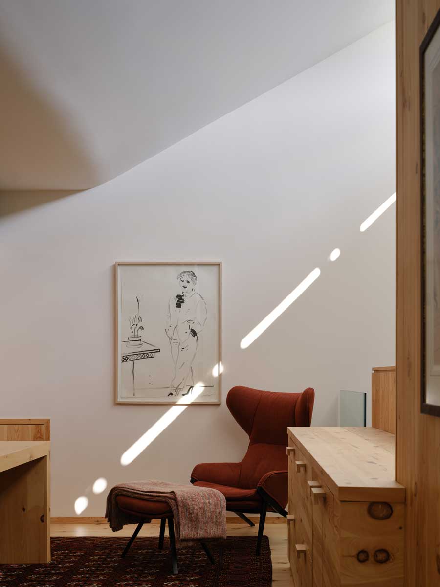 Útulný kout s červeným křeslem, dřevěným nábytkem a jemným světlem dopadajícím na stěnu