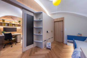 Dětský pokoj s vestavěným nábytkem na míru a pracovním koutem propojený s dalším pokojem posuvnými dveřmi.
