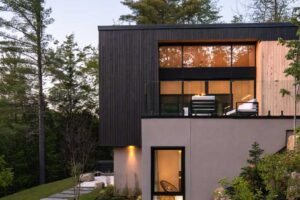 Moderní dům ve svahu večer s osvětlenou terasou a zahradou.