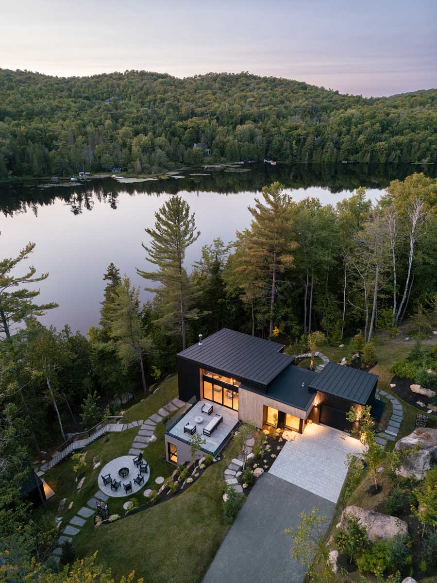 Letecký pohled na dům ve svahu u jezera obklopený lesem a terasami.