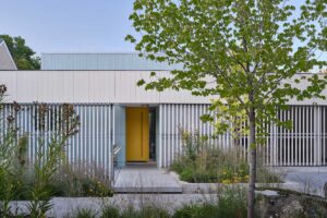 Moderní dům se světlou fasádou, žlutými dveřmi a přírodní zahradou s trvalkami