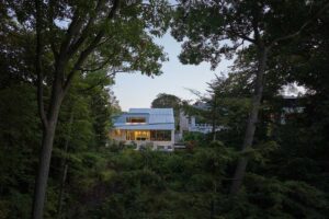 Dům zasazený do zeleného svahu s výhledem do přírodní krajiny a vzrostlých stromů