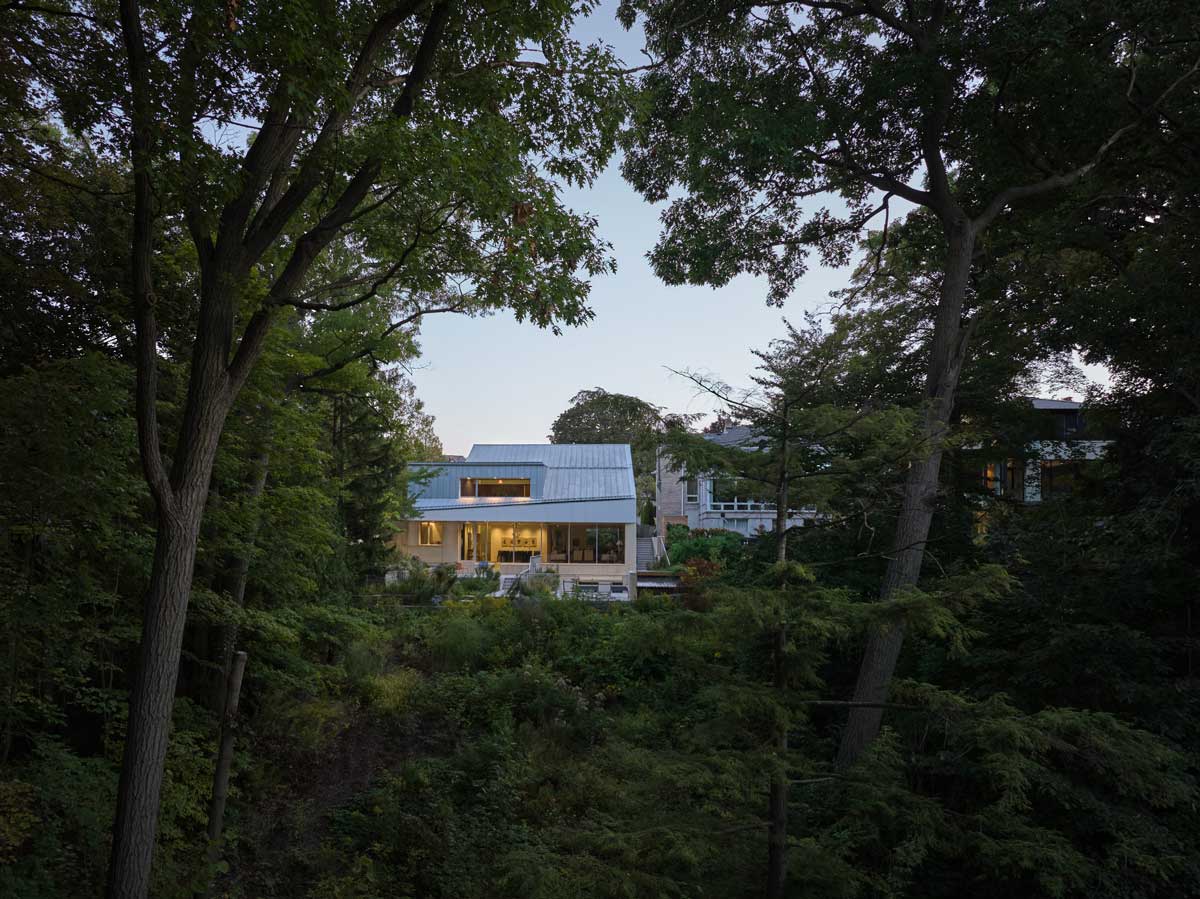 Dům zasazený do zeleného svahu s výhledem do přírodní krajiny a vzrostlých stromů