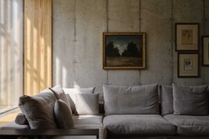 Minimalistický obývací pokoj s betonovou stěnou a světlou sedačkou u velkého okna