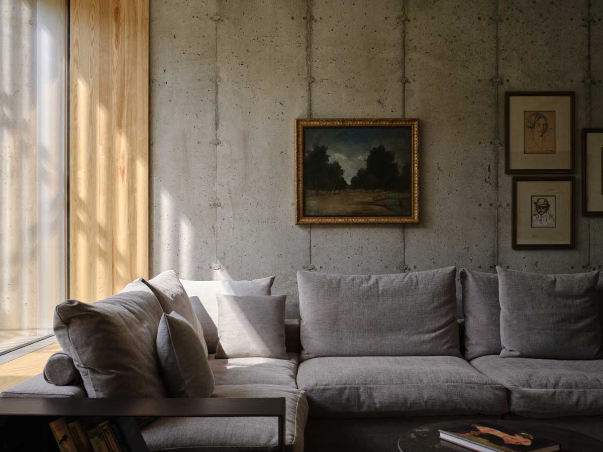 Minimalistický obývací pokoj s betonovou stěnou a světlou sedačkou u velkého okna