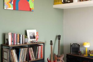 Hudební kout s kytarami vinylovými deskami a policemi na knihy který doplňuje zelená akcentní stěna a historická dlažba.