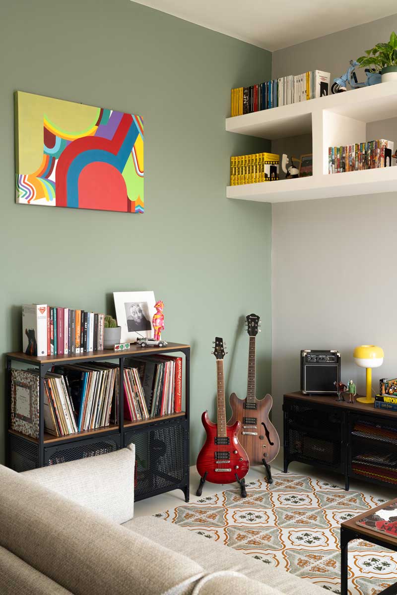 Hudební kout s kytarami vinylovými deskami a policemi na knihy který doplňuje zelená akcentní stěna a historická dlažba.