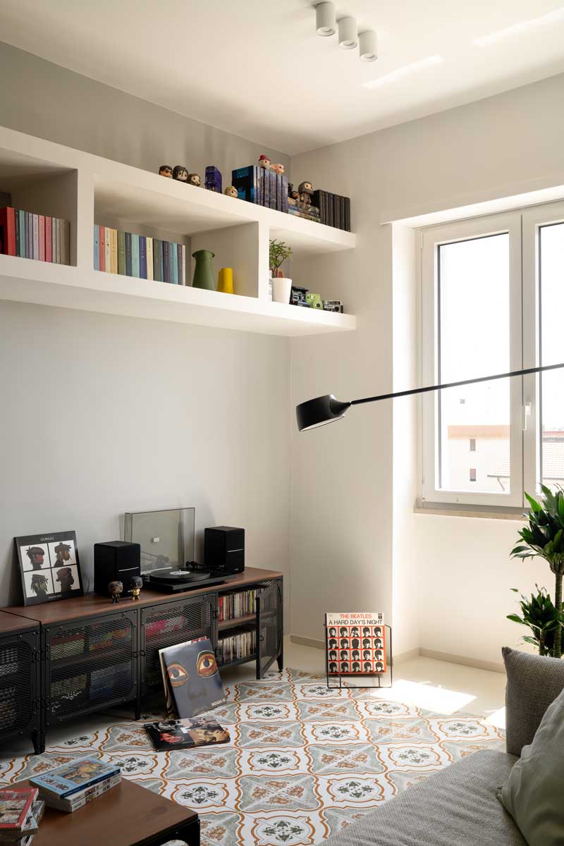 Nízká knihovna s vinylovými deskami gramofonem a dekoracemi umístěná pod vestavěnými policemi v obývací části.