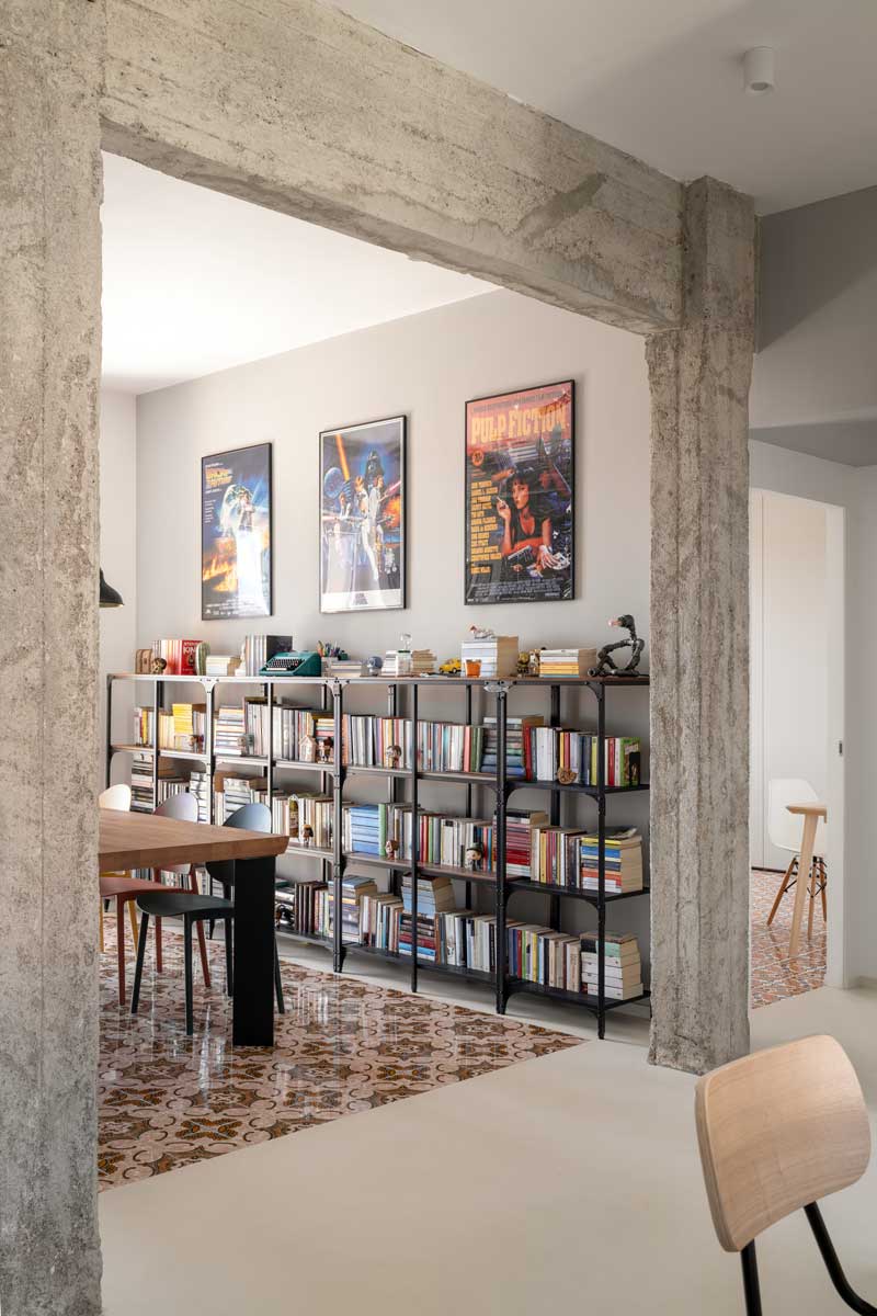 Otevřená knihovna za jídelním stolem která propojuje úložný prostor pro knihy s dekoracemi a filmovými plakáty na stěně.