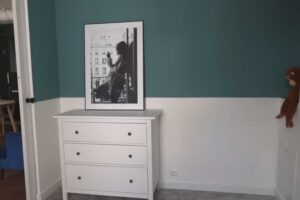 Jednoduchá komoda v dětském pokoji doplněná fotografií a dvoubarevnou výmalbou stěny.