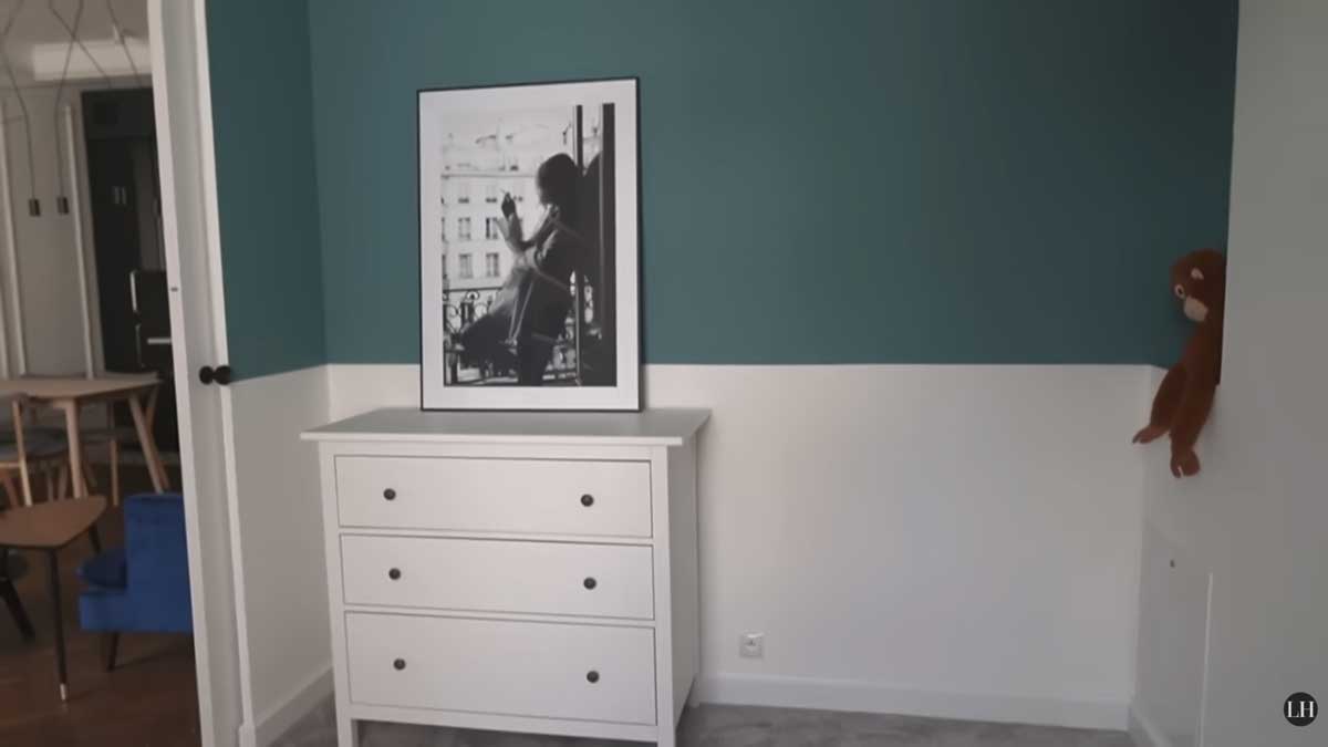 Jednoduchá komoda v dětském pokoji doplněná fotografií a dvoubarevnou výmalbou stěny.