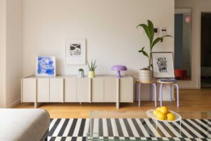Nízká komoda v obývacím prostoru je doplněná minimalistickými dekoracemi, rostlinami a jemnými pastelovými doplňky.