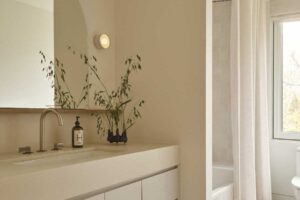 Světlá minimalistická koupelna s oblým zrcadlem a jemnými přírodními doplňky působí klidně a harmonicky