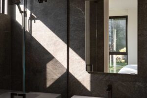 Moderní koupelna s tmavým obkladem, sprchovým koutem a minimalistickým umyvadlem.