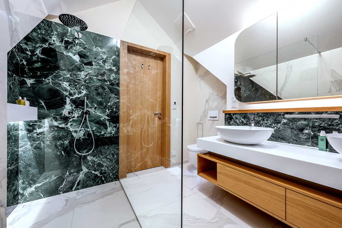 Moderní koupelna s keramickým obkladem v dekoru tmavého kamene a na míru vyrobeným nábytkem v kombinaci dřeva a bílé barvy.