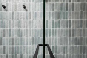 Detail sprchového koutu s jemnou strukturou obkladů a černými armaturami působí minimalisticky.