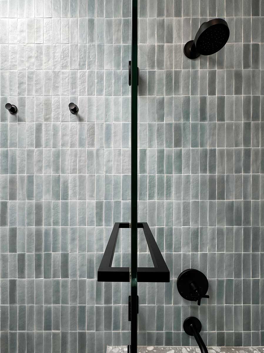 Detail sprchového koutu s jemnou strukturou obkladů a černými armaturami působí minimalisticky.