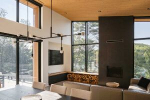 Obývací pokoj s krbem a velkoformátovými okny s výhledem na jezero a les.