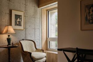 Útulné zákoutí s křeslem, lampou a betonovou stěnou u okna s výhledem ven