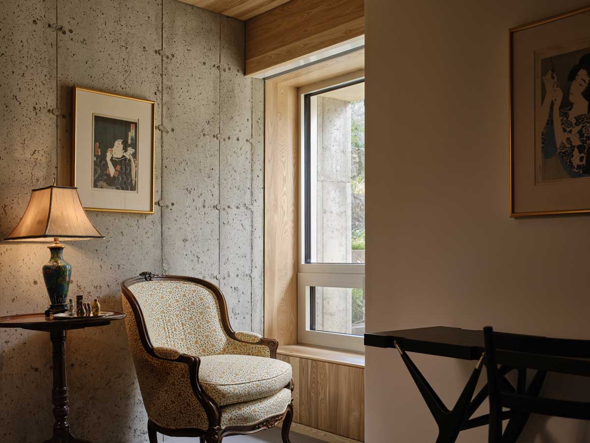 Útulné zákoutí s křeslem, lampou a betonovou stěnou u okna s výhledem ven