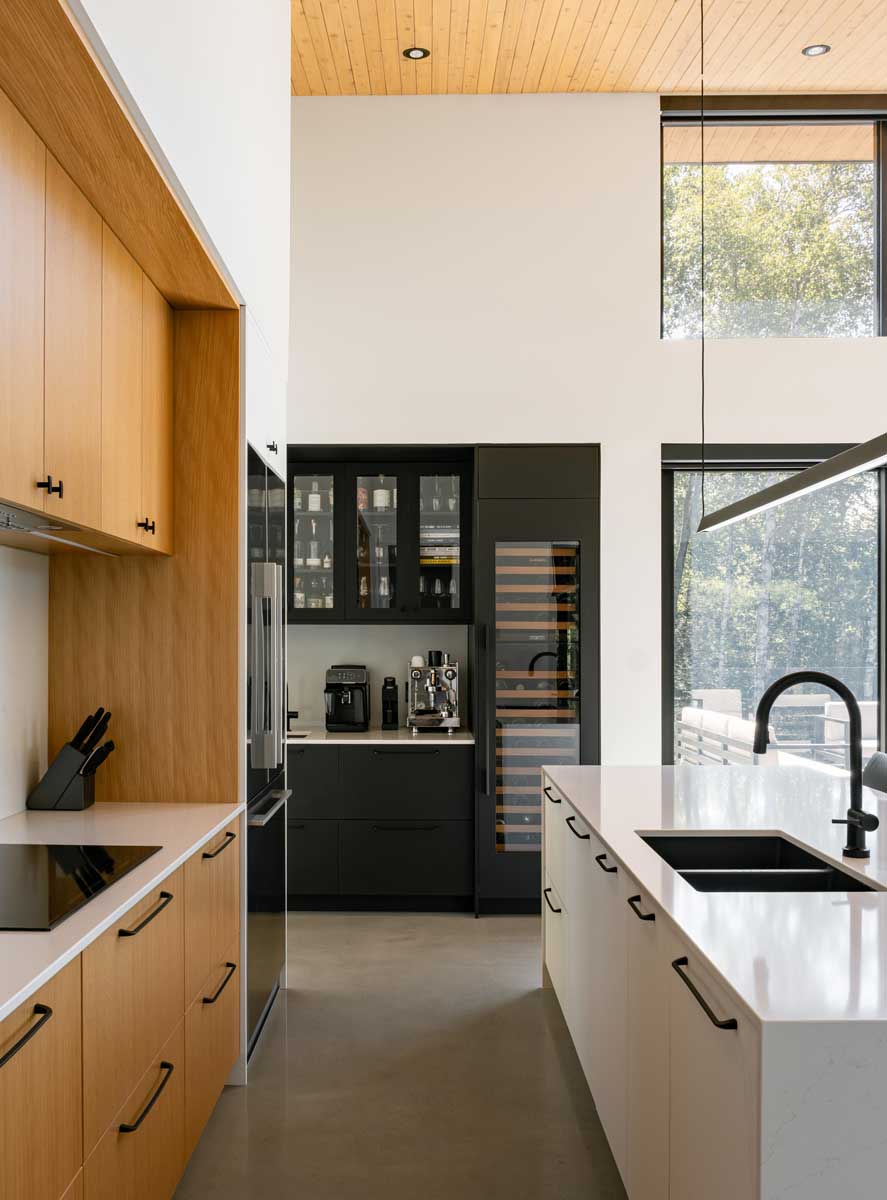 Moderní kuchyň s kombinací dřeva, bílých ploch a vysokým stropem se světlem.