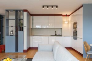 Bílá kuchyňská linka v lesklém provedení je doplněna vínově červenými detaily, které jí dodávají výraznější charakter.