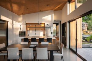 Otevřený interiér s jídelnou, kuchyní a vysokým stropem s velkými okny.