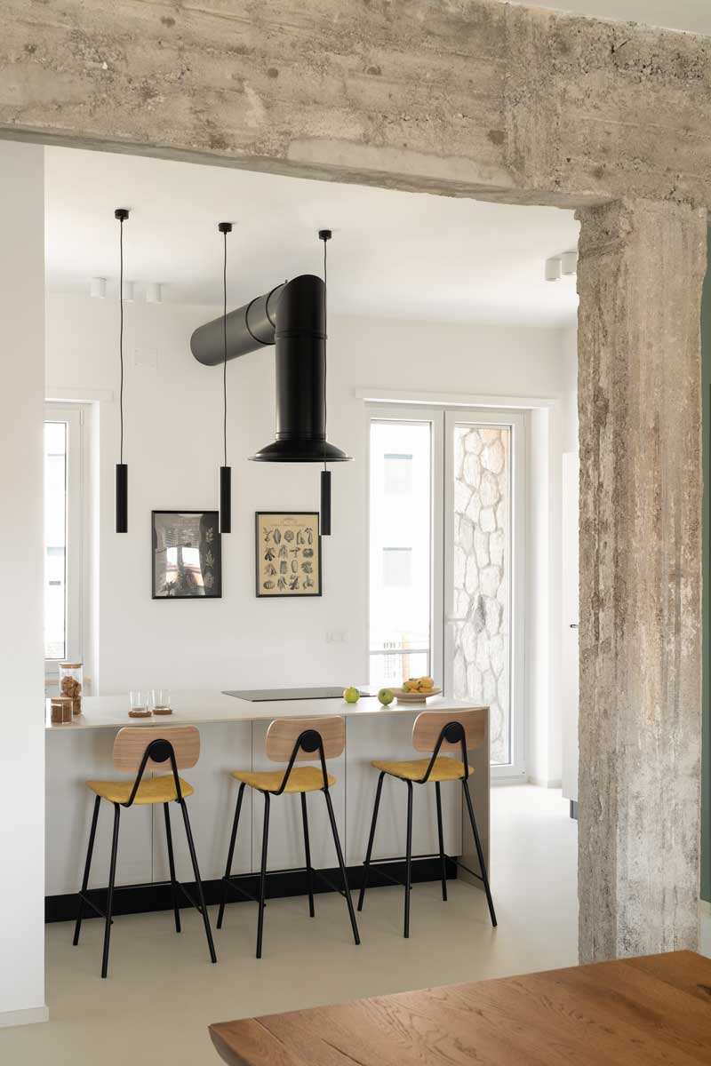 Minimalistická kuchyně s ostrůvkem doplněná ručně vyráběnou kovovou digestoří a subtilními závěsnými svítidly nad pracovní plochou.