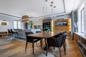 Otevřený prostor kuchyně a jídelny s dřevěnou podlahou ve vzoru stromečku a elegantním jídelním stolem.