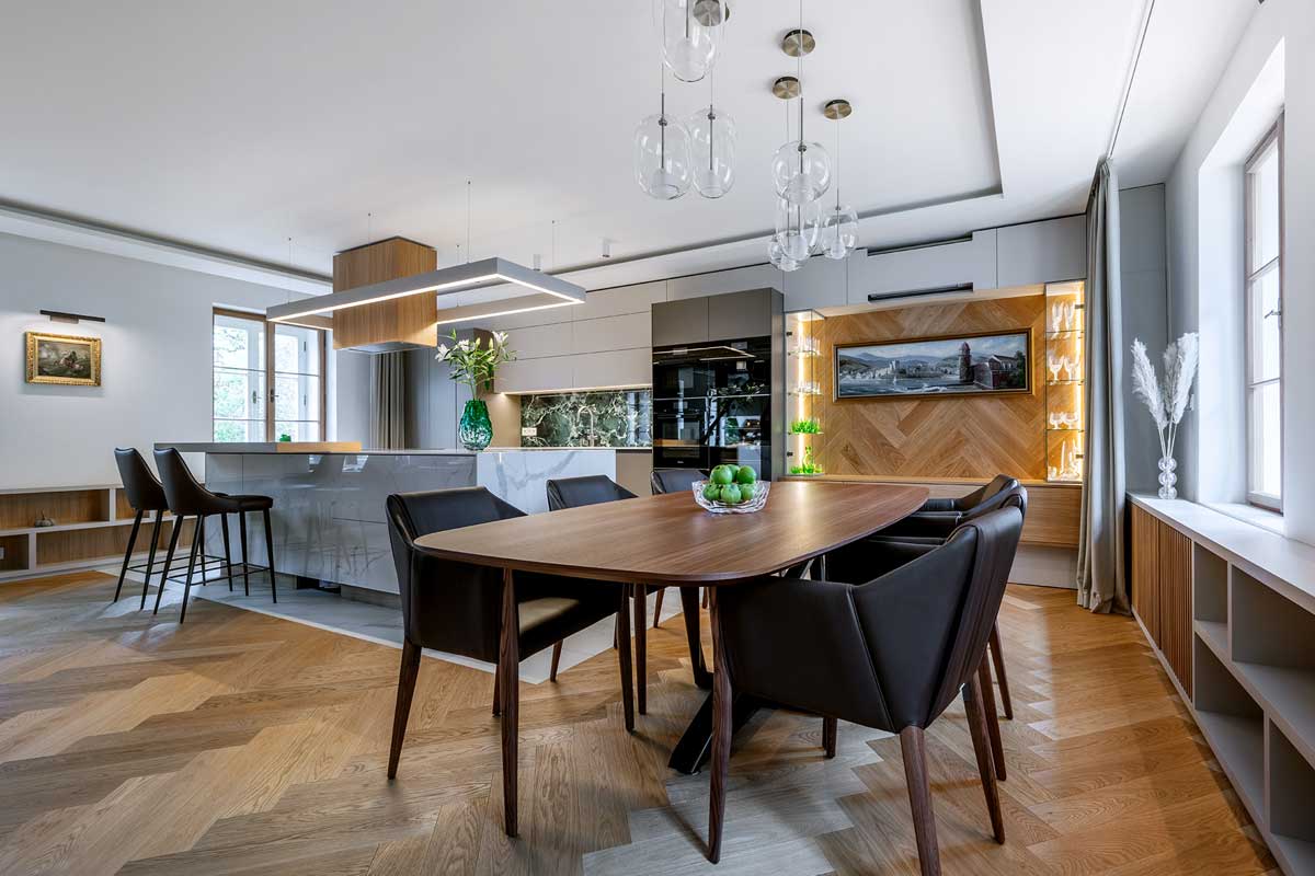 Otevřený prostor kuchyně a jídelny s dřevěnou podlahou ve vzoru stromečku a elegantním jídelním stolem.