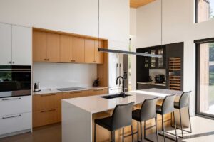 Kuchyň s ostrůvkem a barovými židlemi v moderním interiéru s dřevěnými prvky.