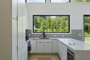 Minimalistická kuchyň s čistými liniemi a velkým oknem přivádějícím do prostoru dostatek denního světla.