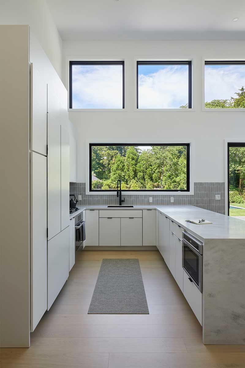 Minimalistická kuchyň s čistými liniemi a velkým oknem přivádějícím do prostoru dostatek denního světla.