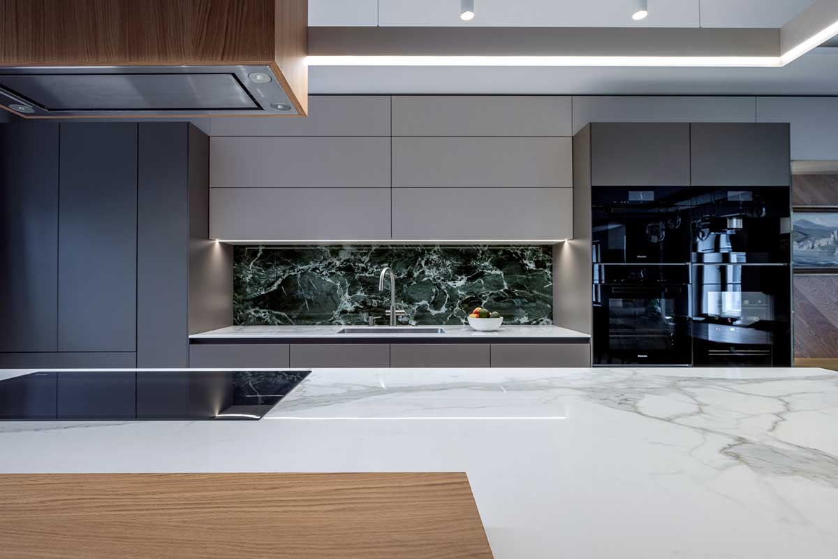 Minimalistická kuchyňská linka s kamenným dekorem obkladu a integrovanými spotřebiči v tmavém provedení.
